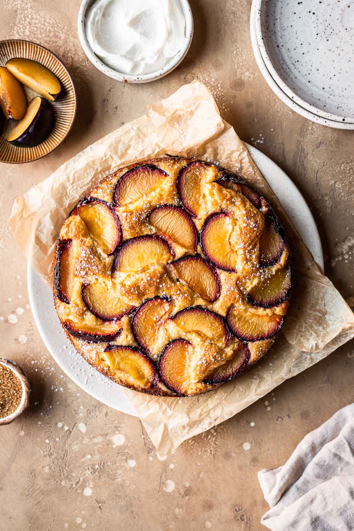 A baked plum yogurt cake on a parchment paper lined platter.