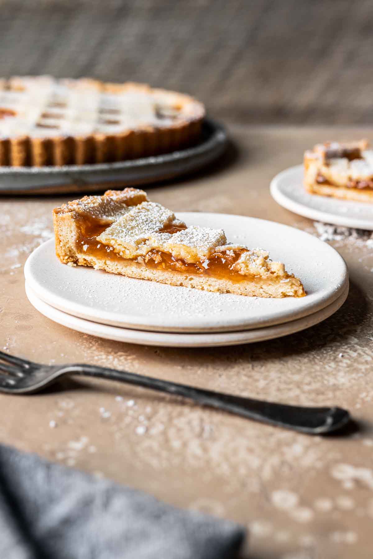 A slice of lattice topped apricot jam tart on a plate.