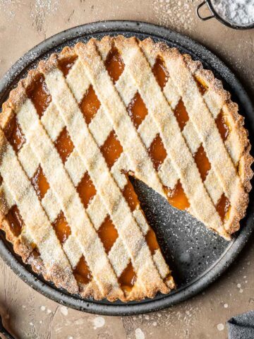 A lattice topped crostata di marmellata with one slice removed.