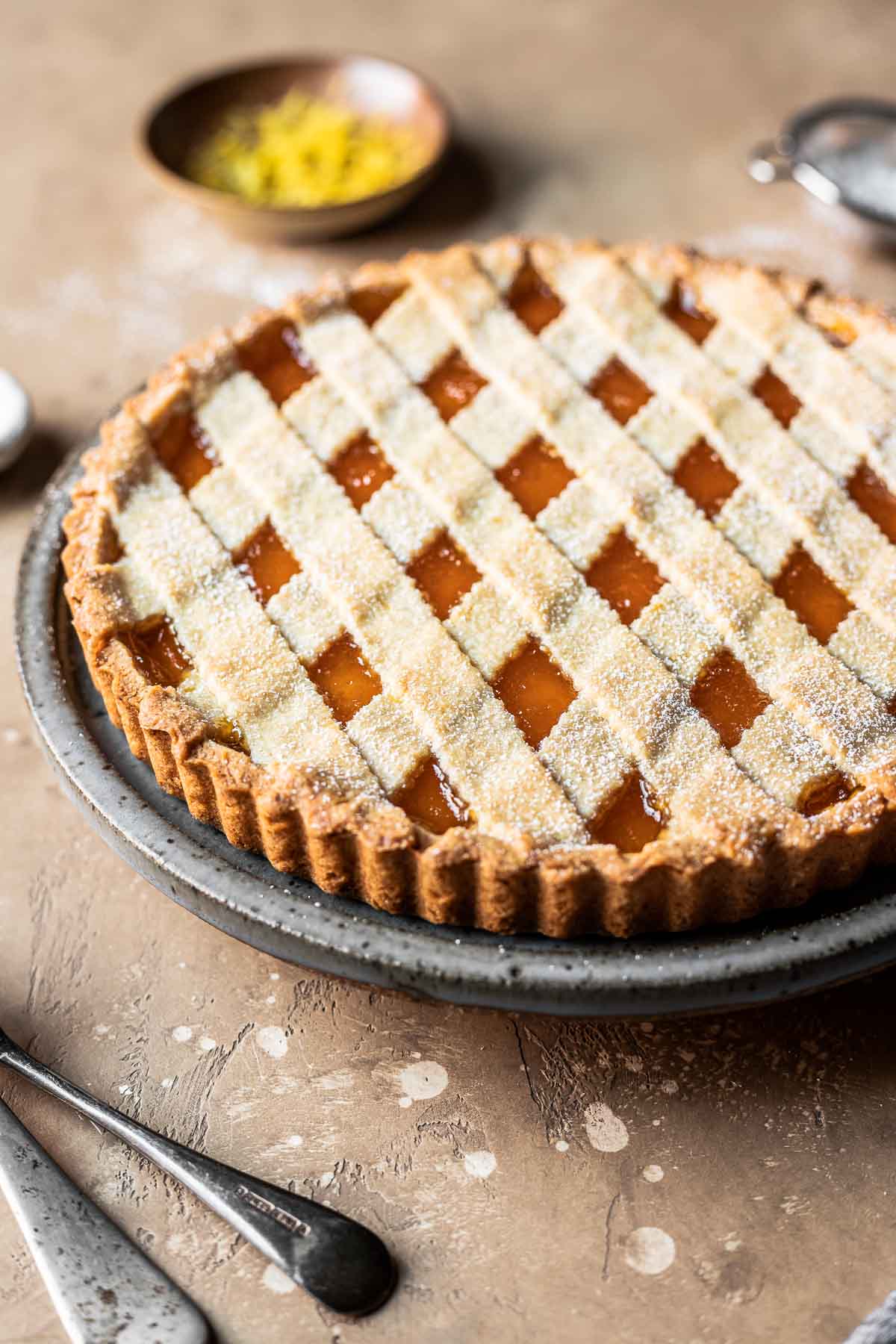 A lattice topped crostata di marmellata on a grey speckled plate.