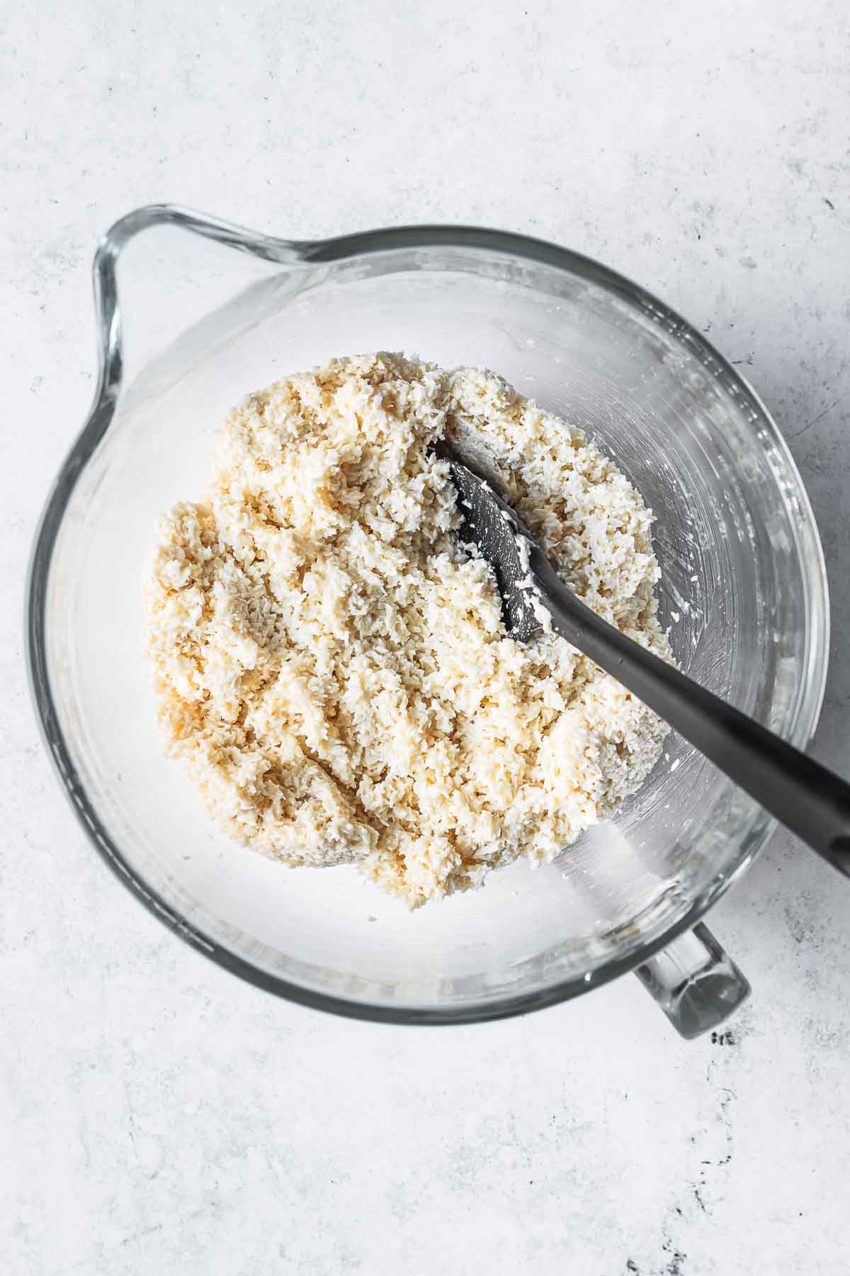 Dough for coconut macaroons in a clear glass mixing bowl.