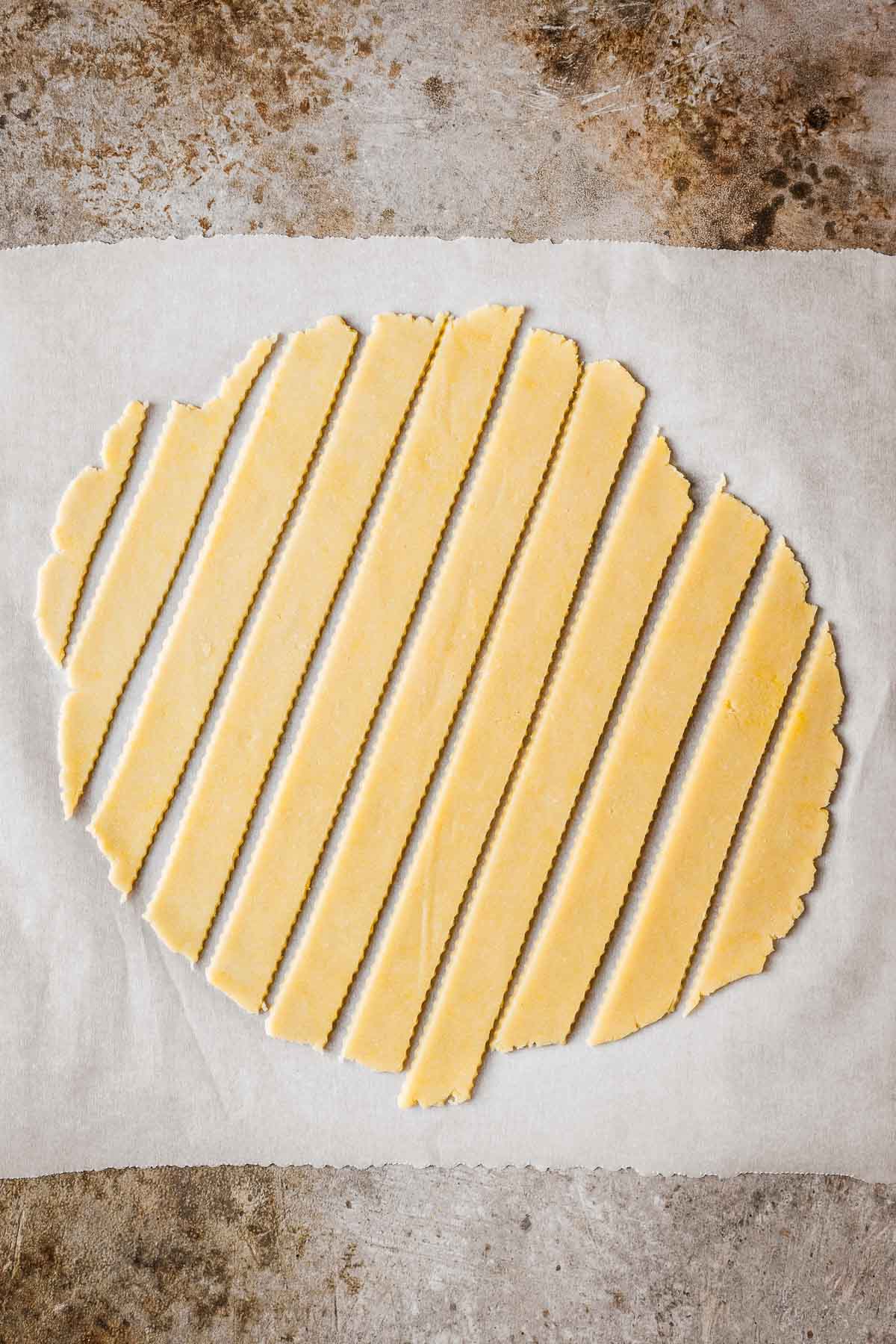 Fluted strips of lattice dough on a sheet of parchment paper.