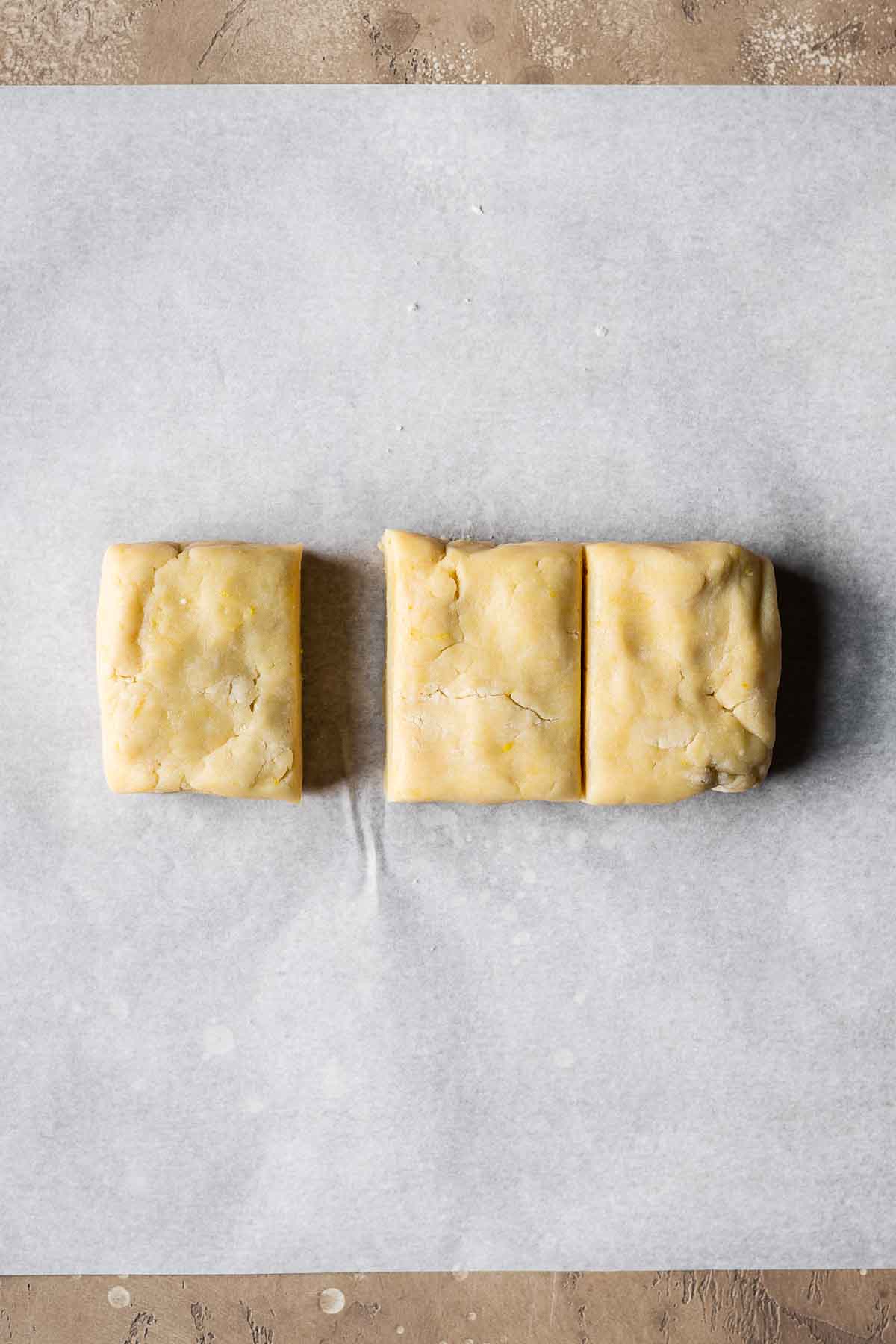 Shortcrust pastry dough divided into thirds on parchment paper.