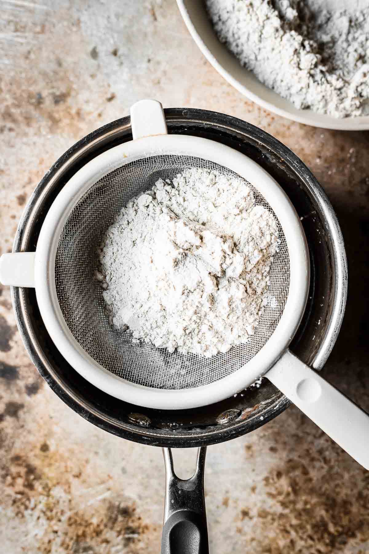A sieve of flour over a saucepan of cookie batter.