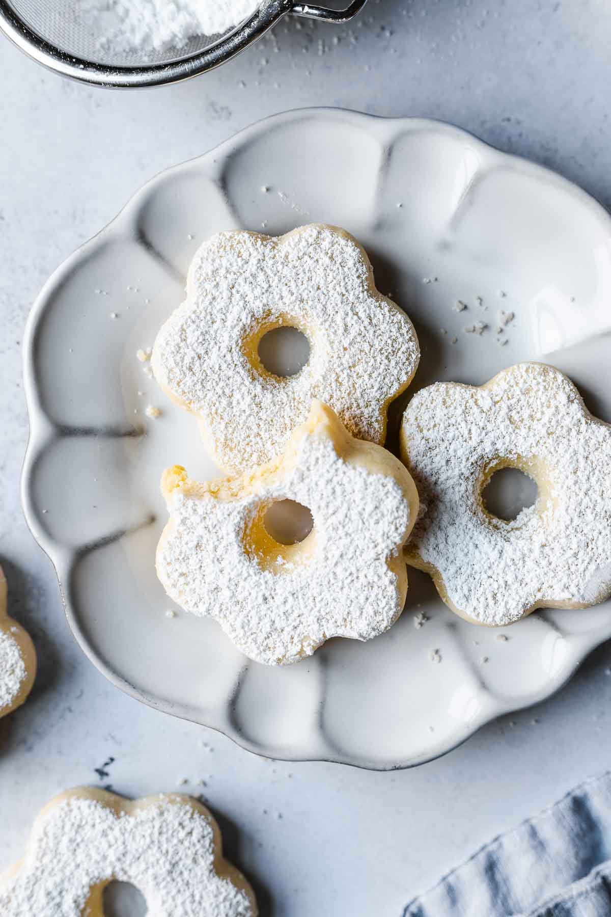 Three flower shaped cookies on a white fluted plate.