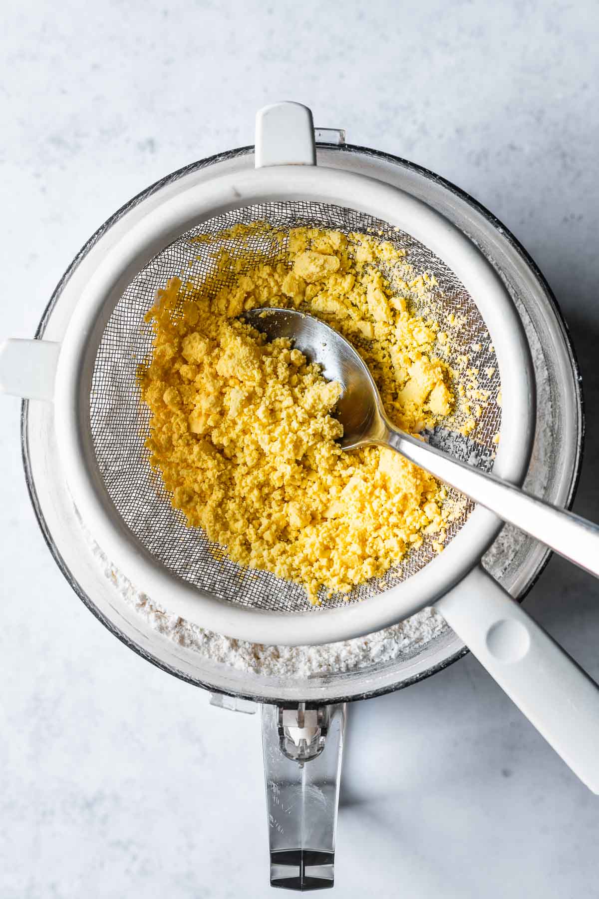 A spoon pressing hard boiled egg yolks through a strainer.