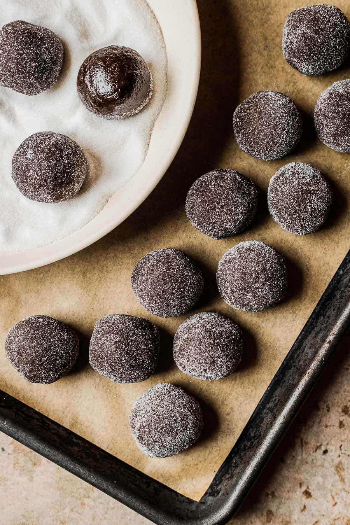Balls of chocolate cookie dough rolled in sugar on a baking sheet.