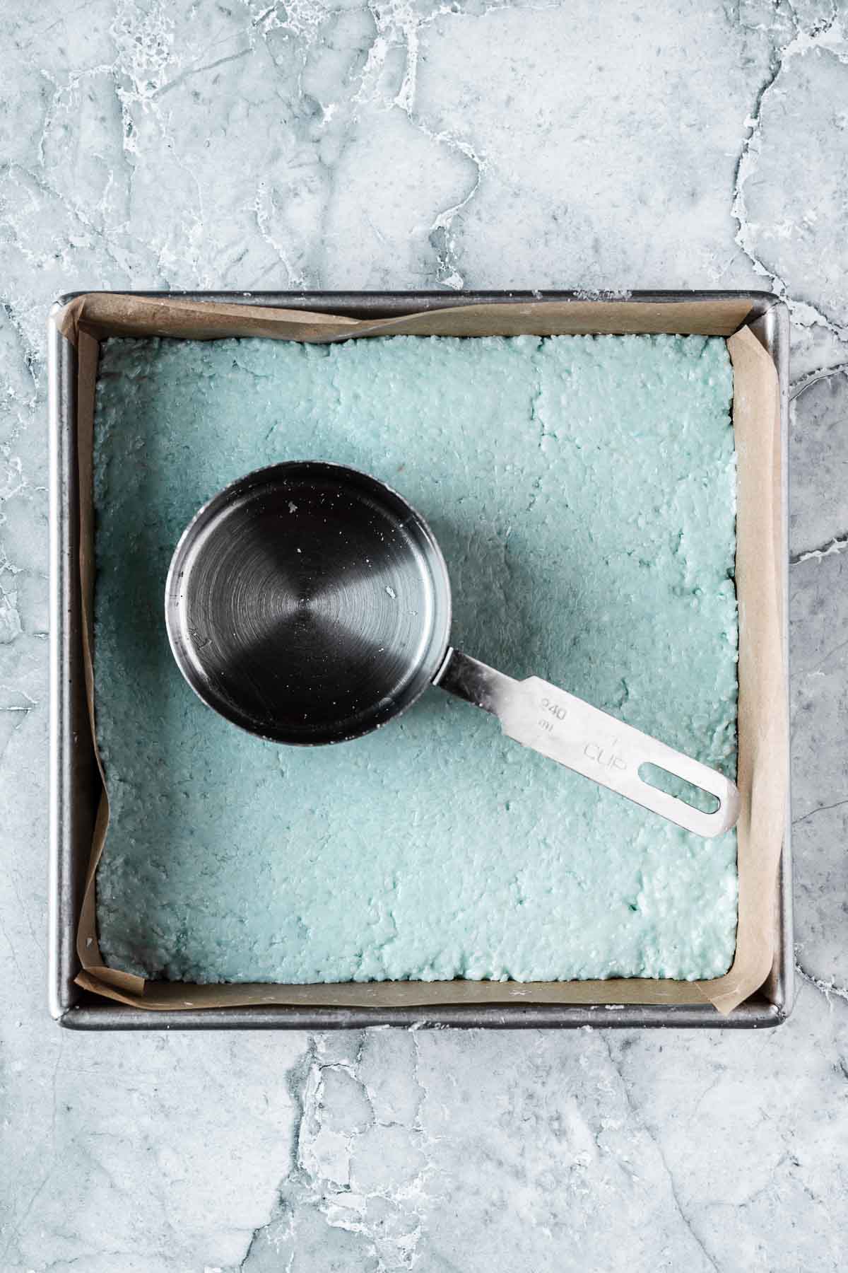 The blue top layer of candy being compacted with a measuring cup.