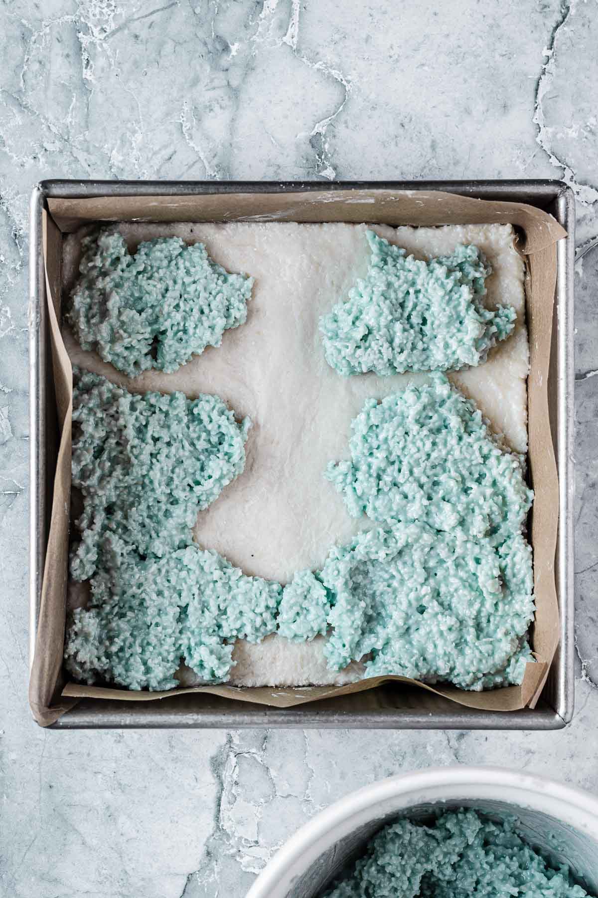 The blue layer of coconut ice being placed on top of the white layer.