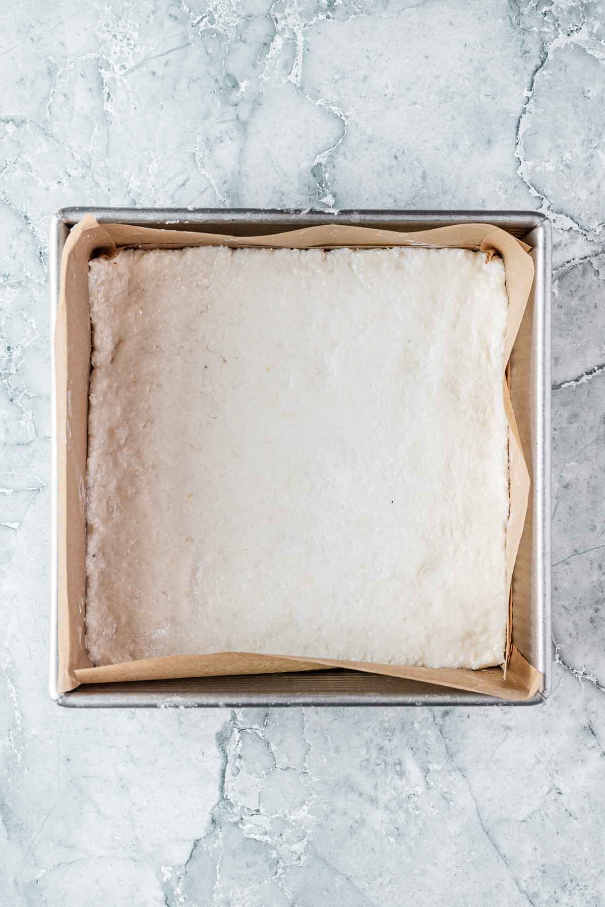 The compacted layer of white coconut ice in a square pan.