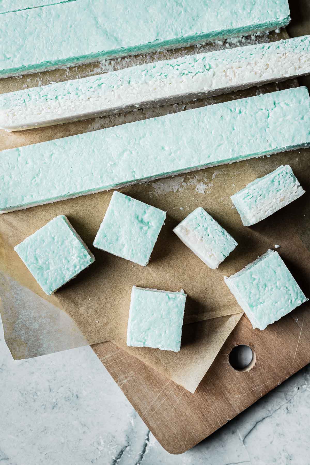 A cutting board with strips of coconut candy being cut into squares.