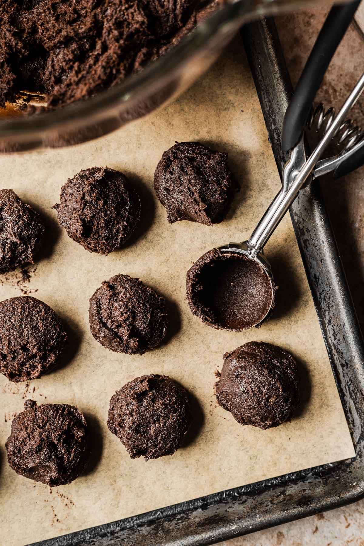 Scoops of chocolate gingerbread cookie dough on a parchment lined cookie sheet.