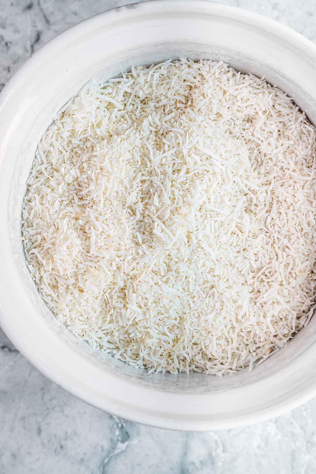 Shredded coconut in a white bowl before being chopped fine.