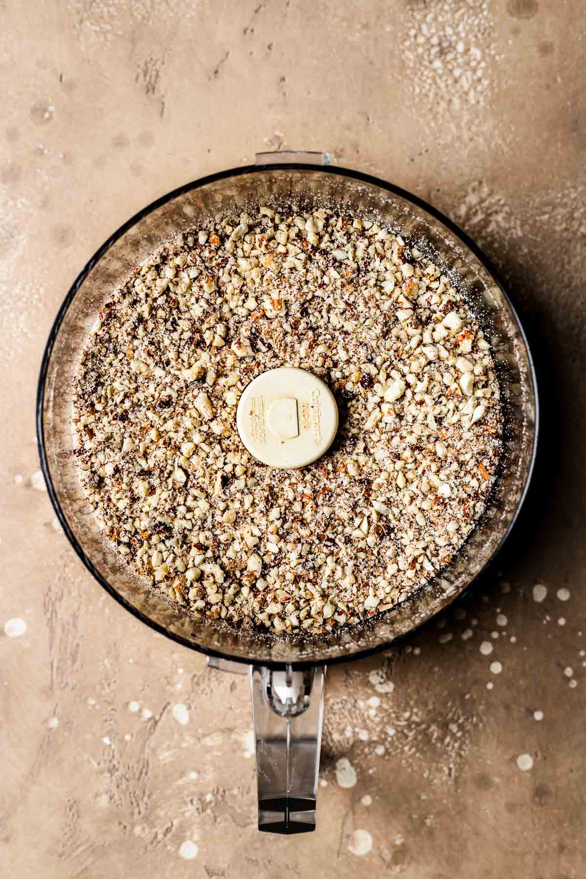 A food processor bowl with finely chopped almonds and hazelnuts.
