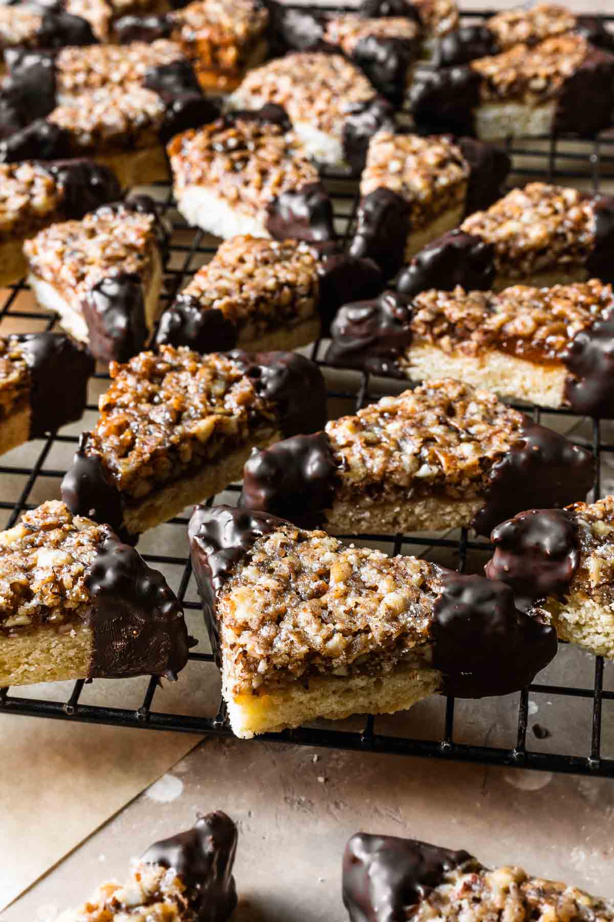 Triangular shortbread cookies with nut topping and chocolate dipped corners on a cookie rack.