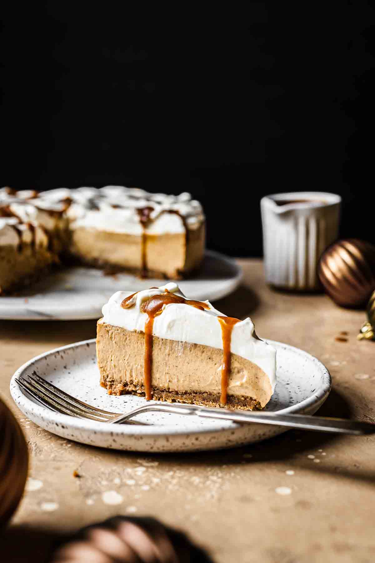 A slice of gingerbread cheesecake topped with whipped cream and caramel sauce on a white plate.