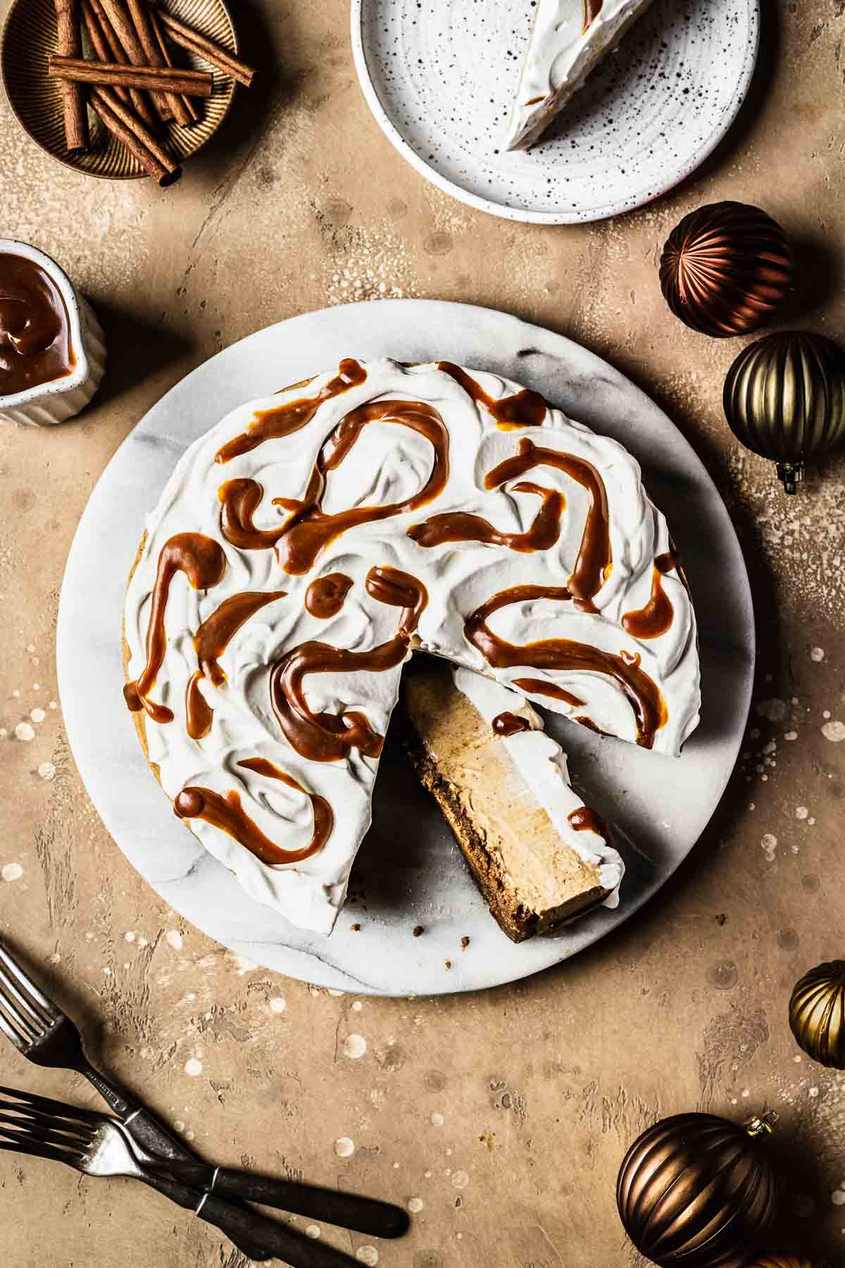 Gingerbread cheesecake topped with whipped cream and caramel sauce, with a slice on its side to show the layers.