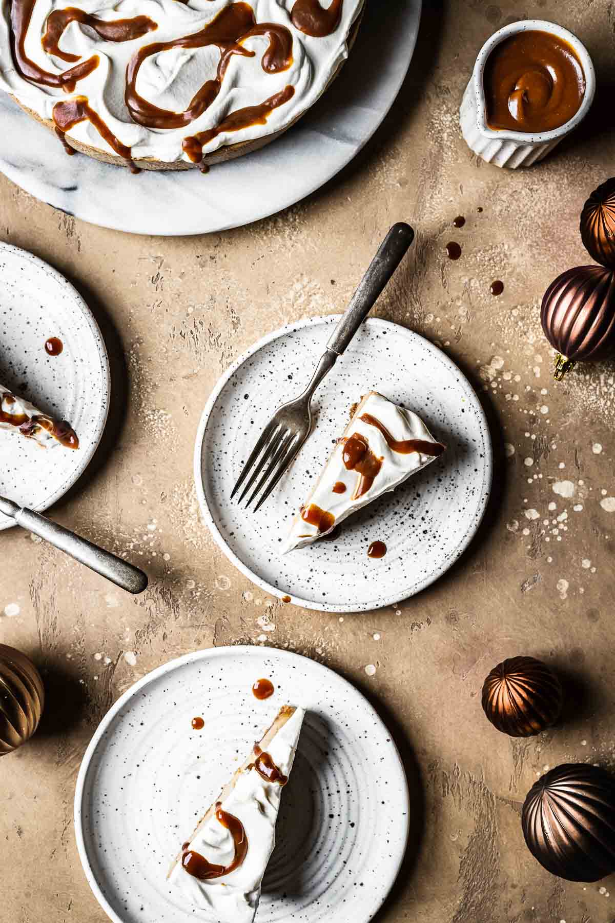 Slices of whipped cream and caramel drizzled cheesecake on white ceramic plates.