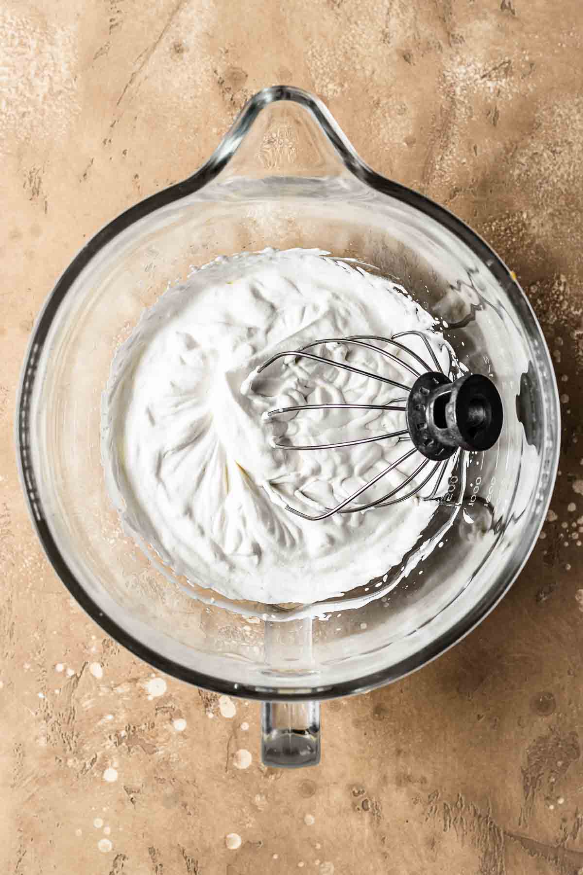Medium firm peaks of whipped cream in a glass mixing bowl.