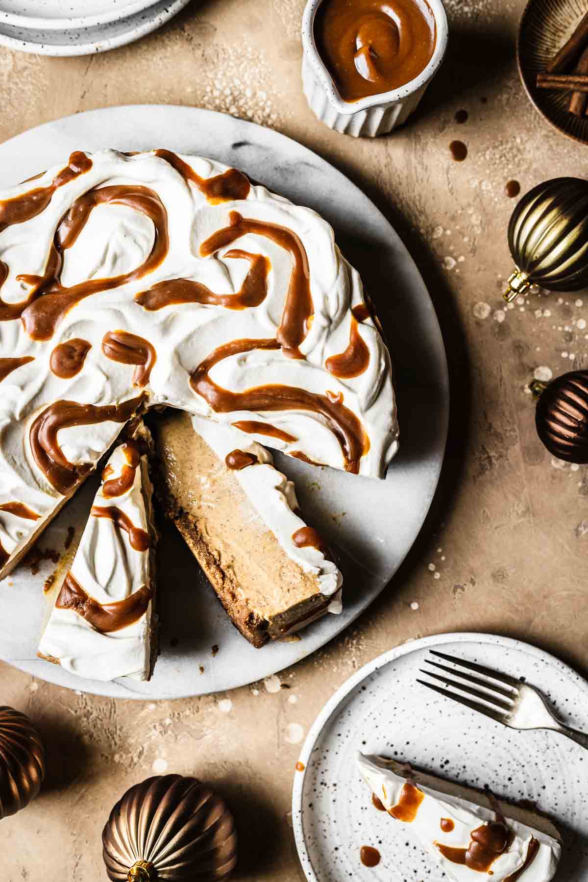 Slices of gingerbread cheesecake on a marble platter with plates and Christmas baubles nearby.