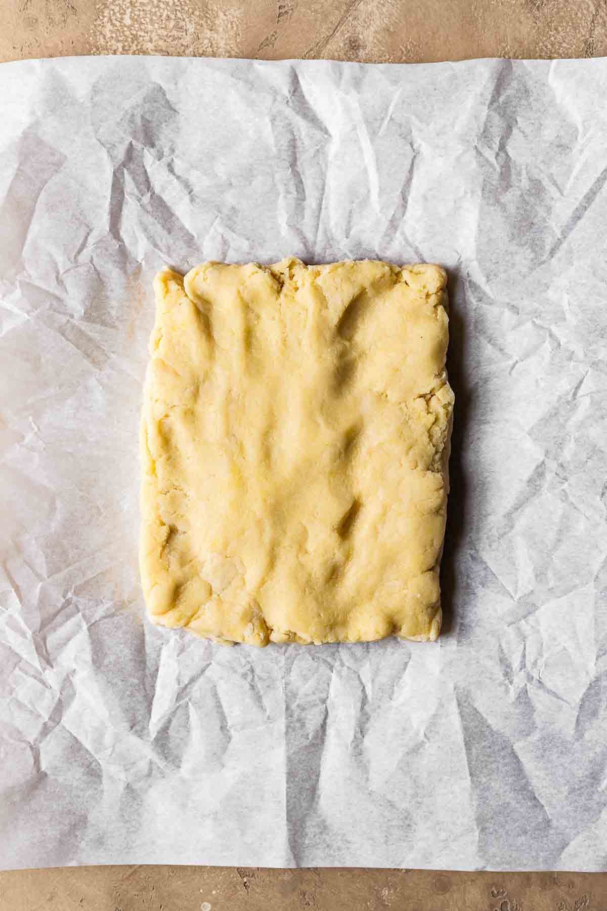 Shortcrust pastry dough for nussecken shaped into rectangle on parchment paper.