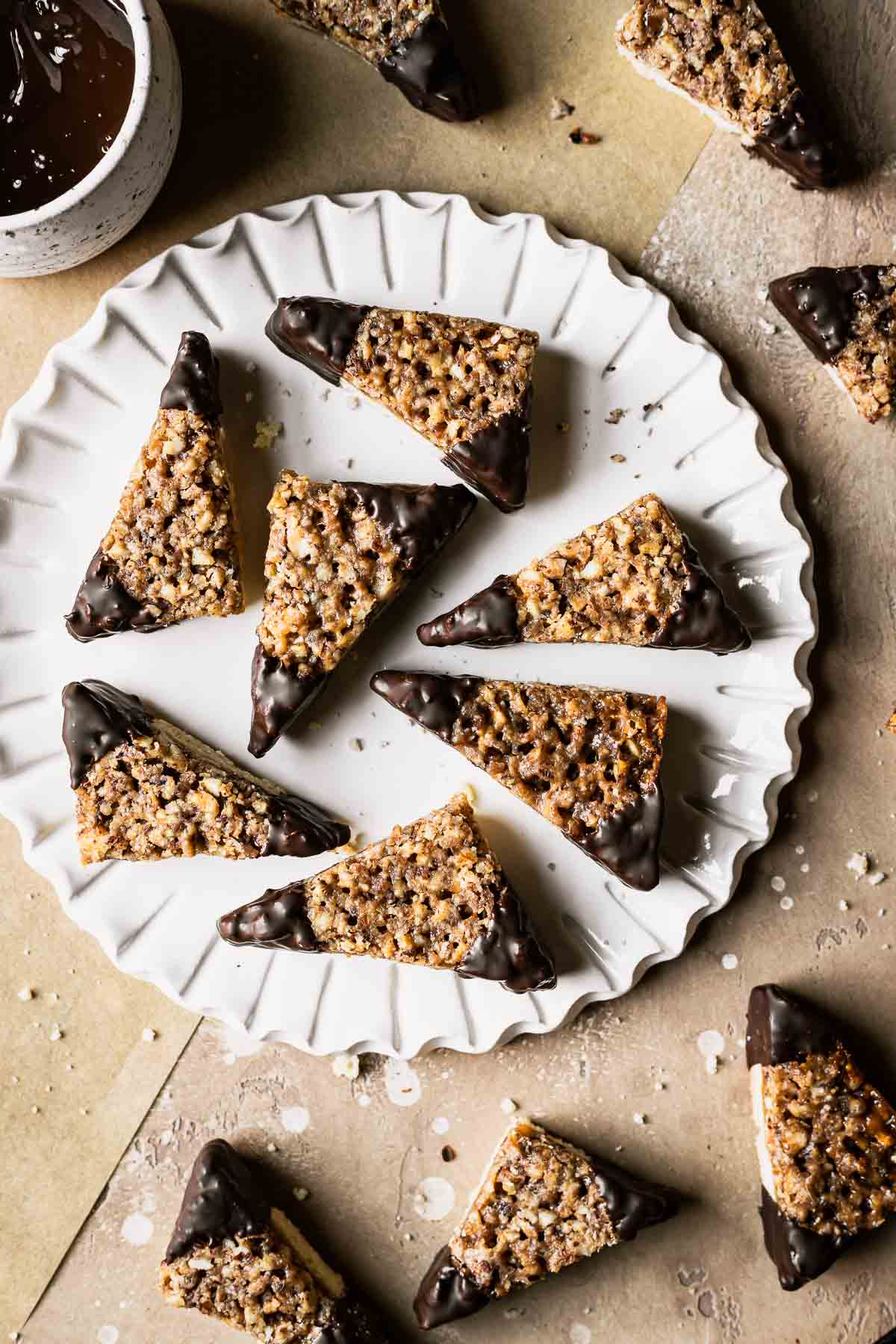 Triangle shaped nut cookies with corners dipped in chocolate on a white ceramic plate.