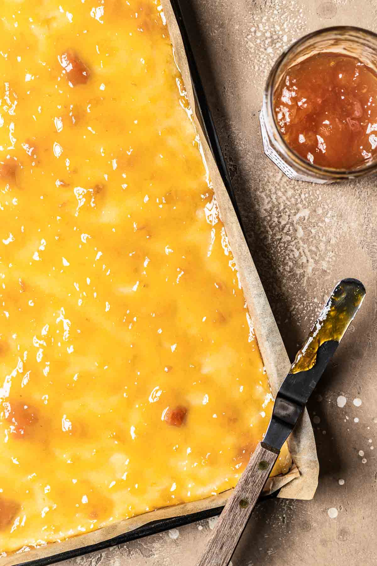 Apricot jam spread over a pan filled with shortcrust pastry dough.