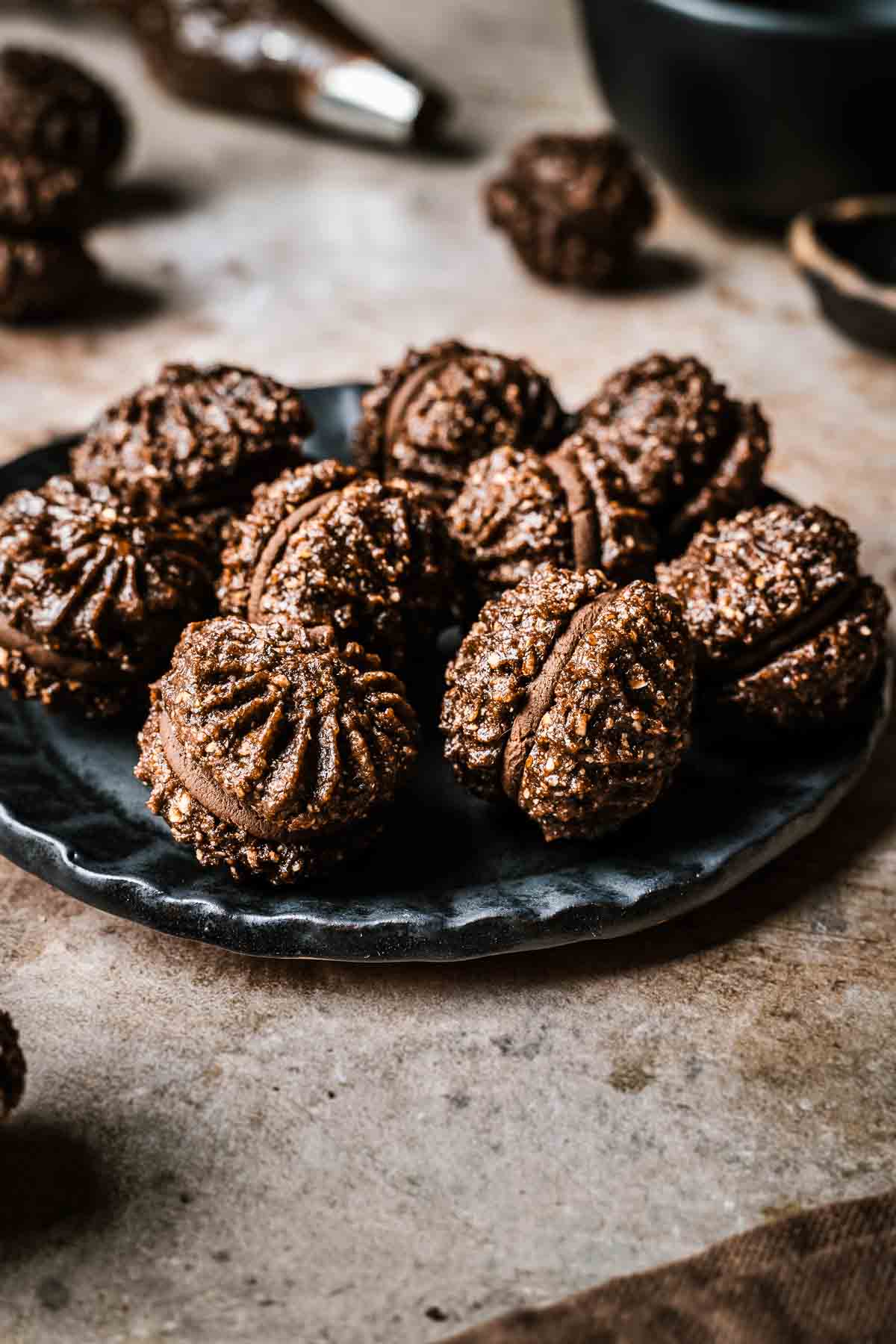 Piped baci di Alassio sandwich cookies on a black ceramic plate.