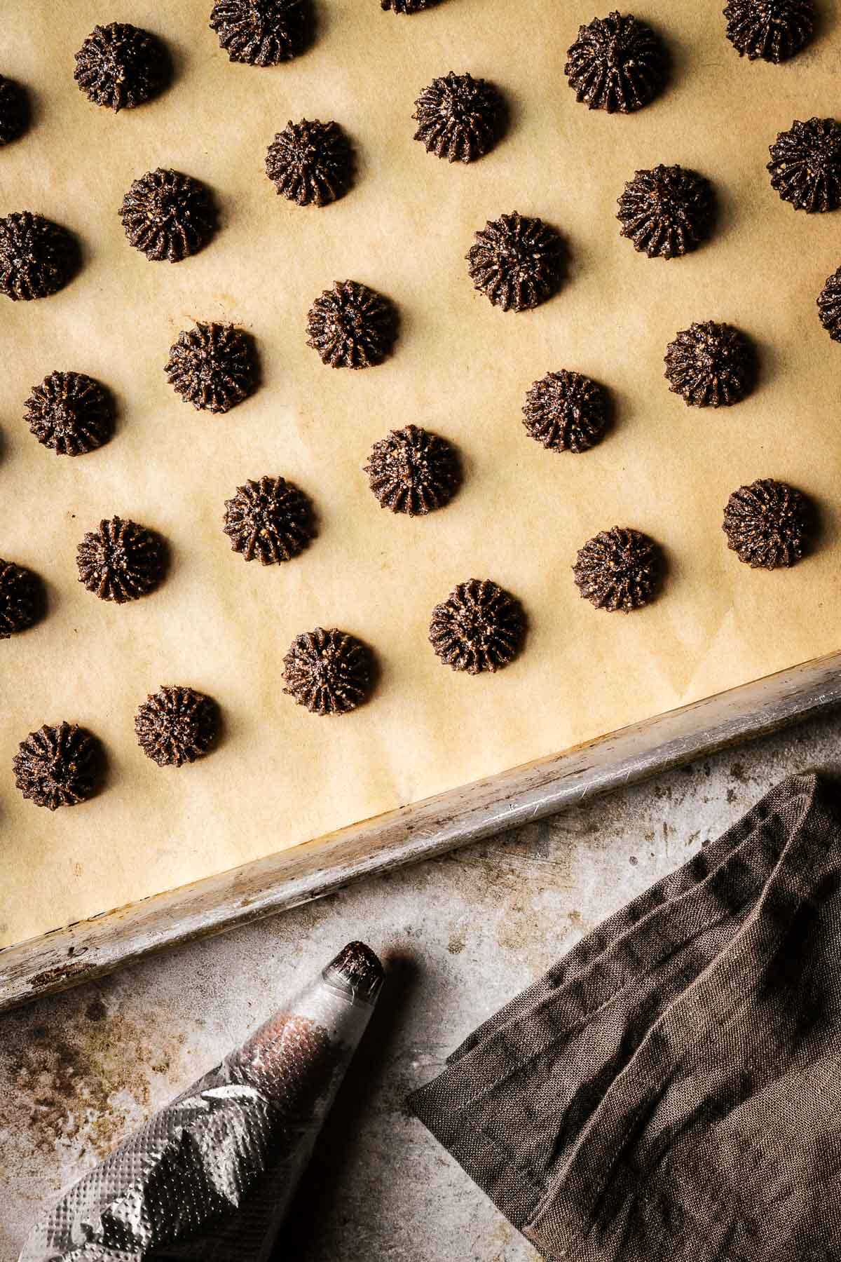 Baci di alassio cookie batter piped in star shapes onto a brown parchment paper lined baking sheet.