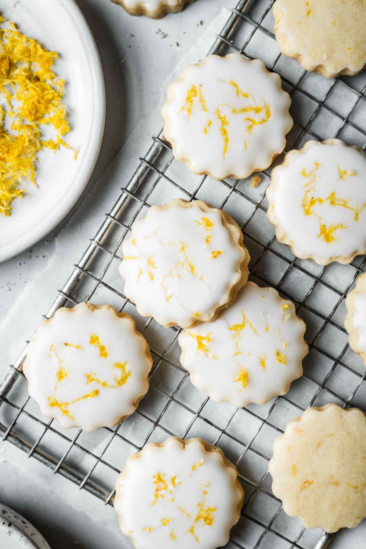 Glazed cookies with lemon zest on a cooling rack.