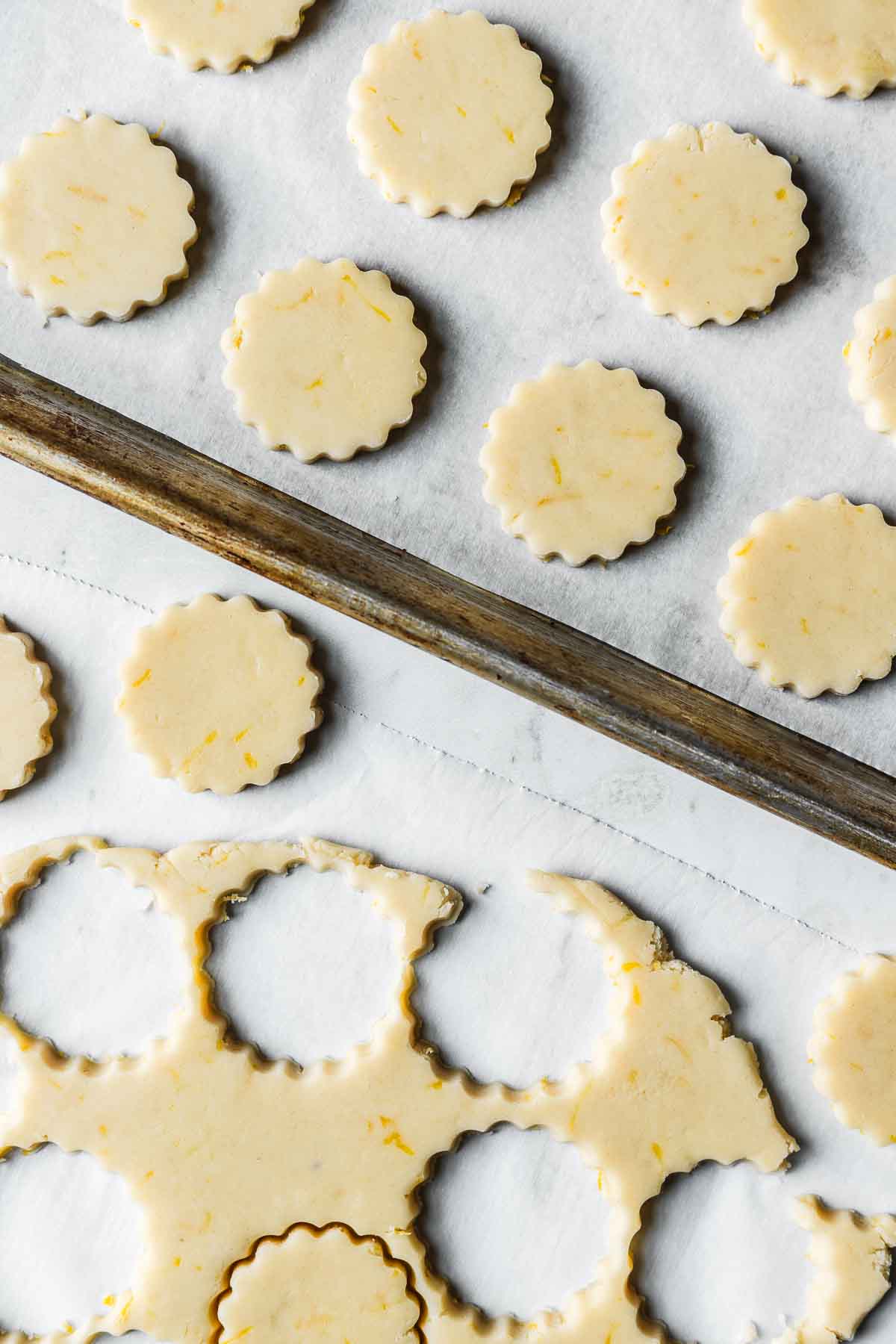 Shortbread cookie cutouts on white parchment paper and a parchment lined baking sheet.
