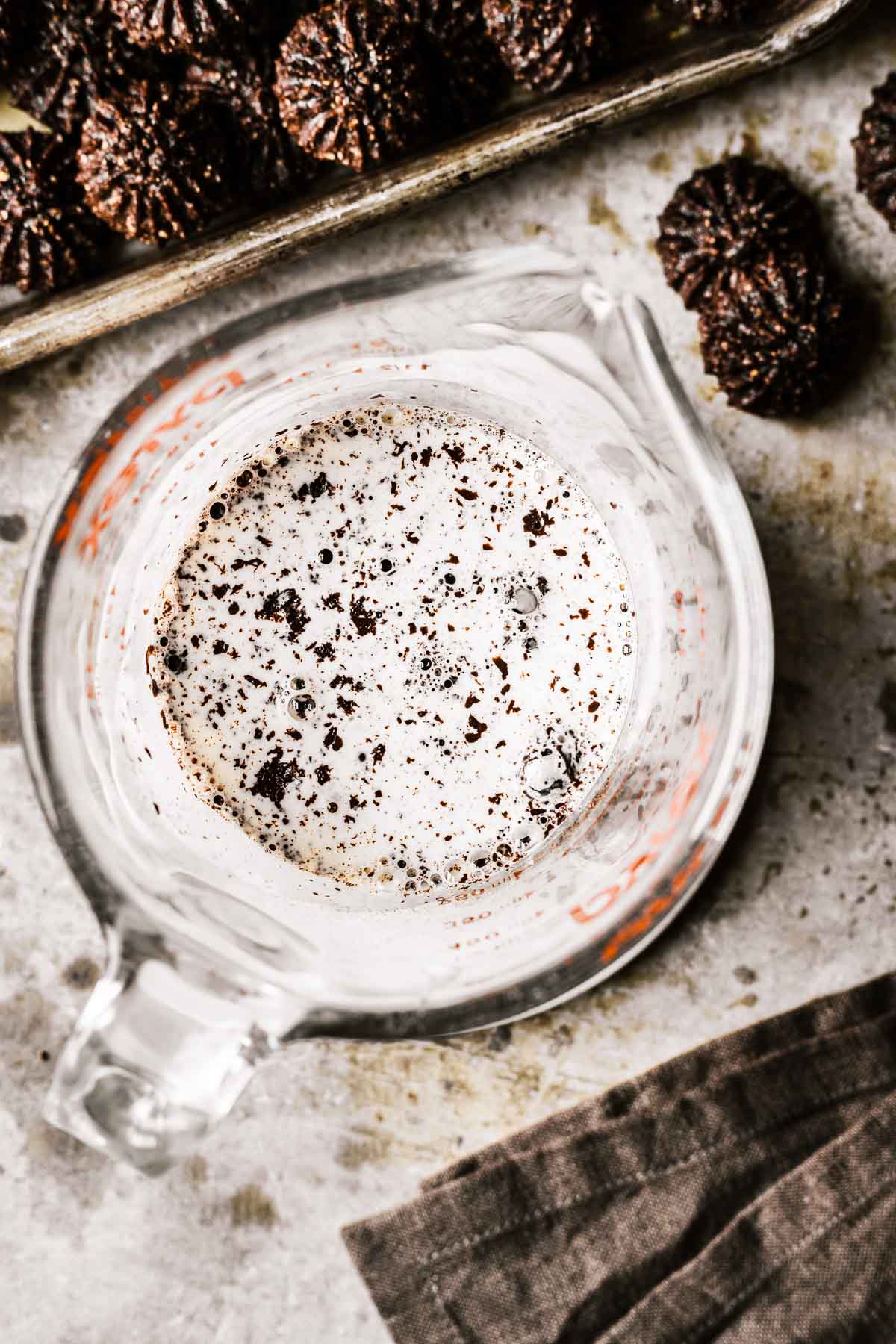 Hot heavy cream and chopped chocolate for ganache in a glass measuring cup.