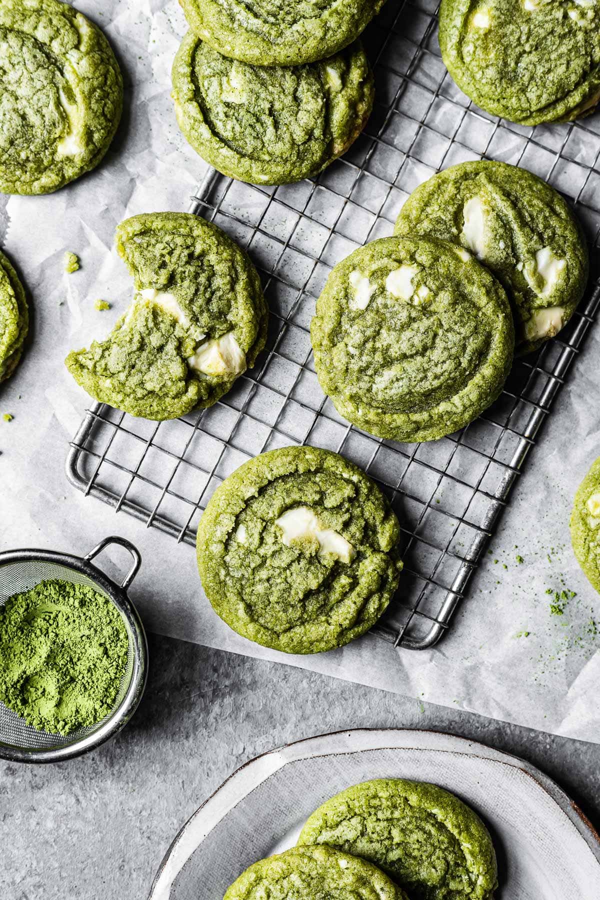 Green matcha white chocolate cookies on a cooling rack resting on white parchment paper.