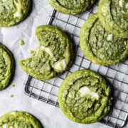 A close up of green drop cookies with white chocolate chunks on a metal cooling rack.