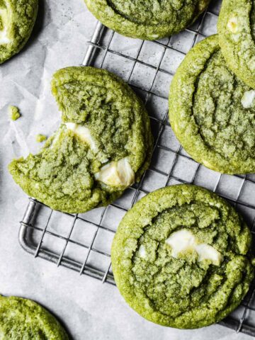 A close up of green drop cookies with white chocolate chunks on a metal cooling rack.