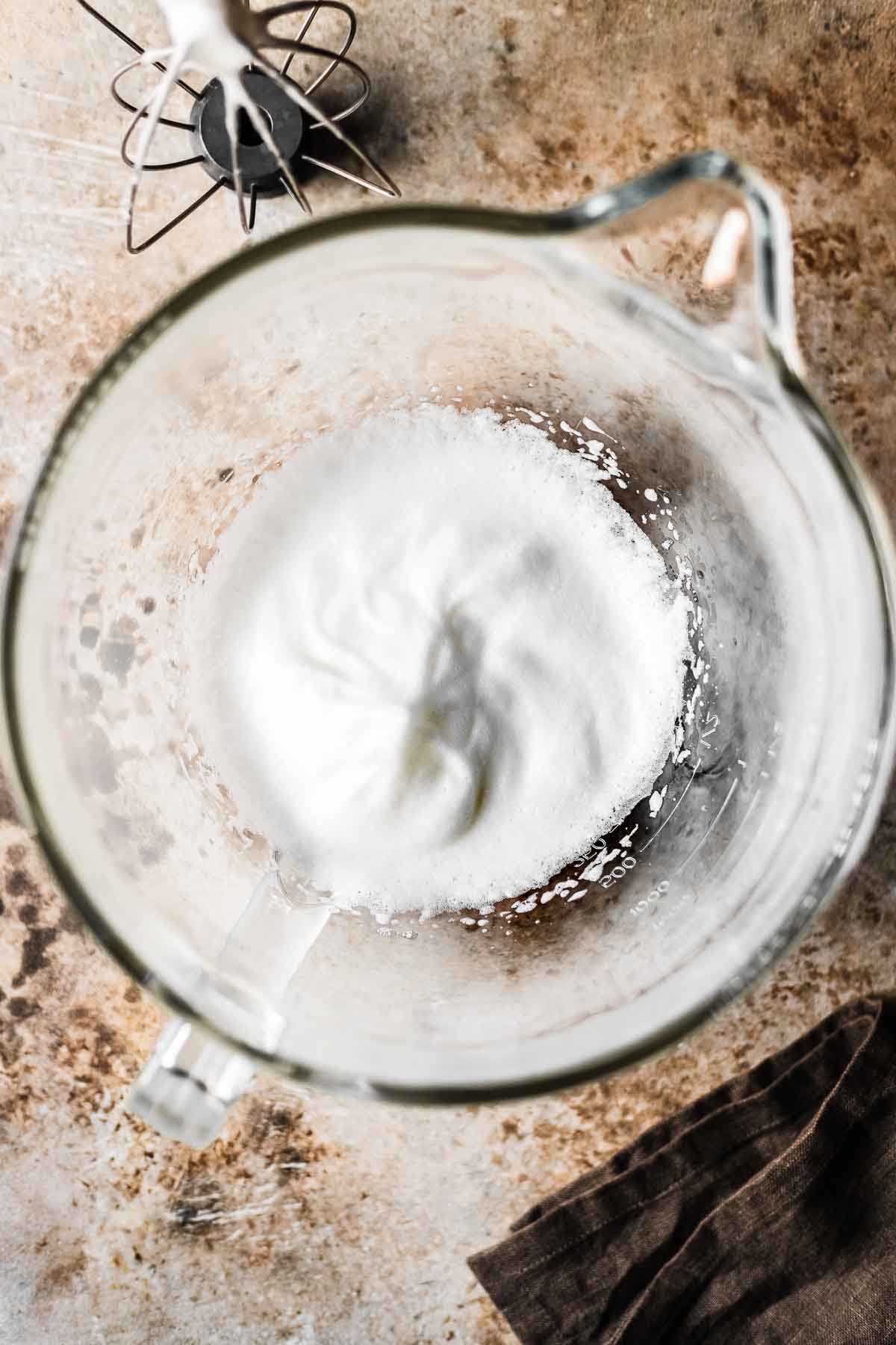 Egg whites beaten to stiff peaks in a clear glass bowl.