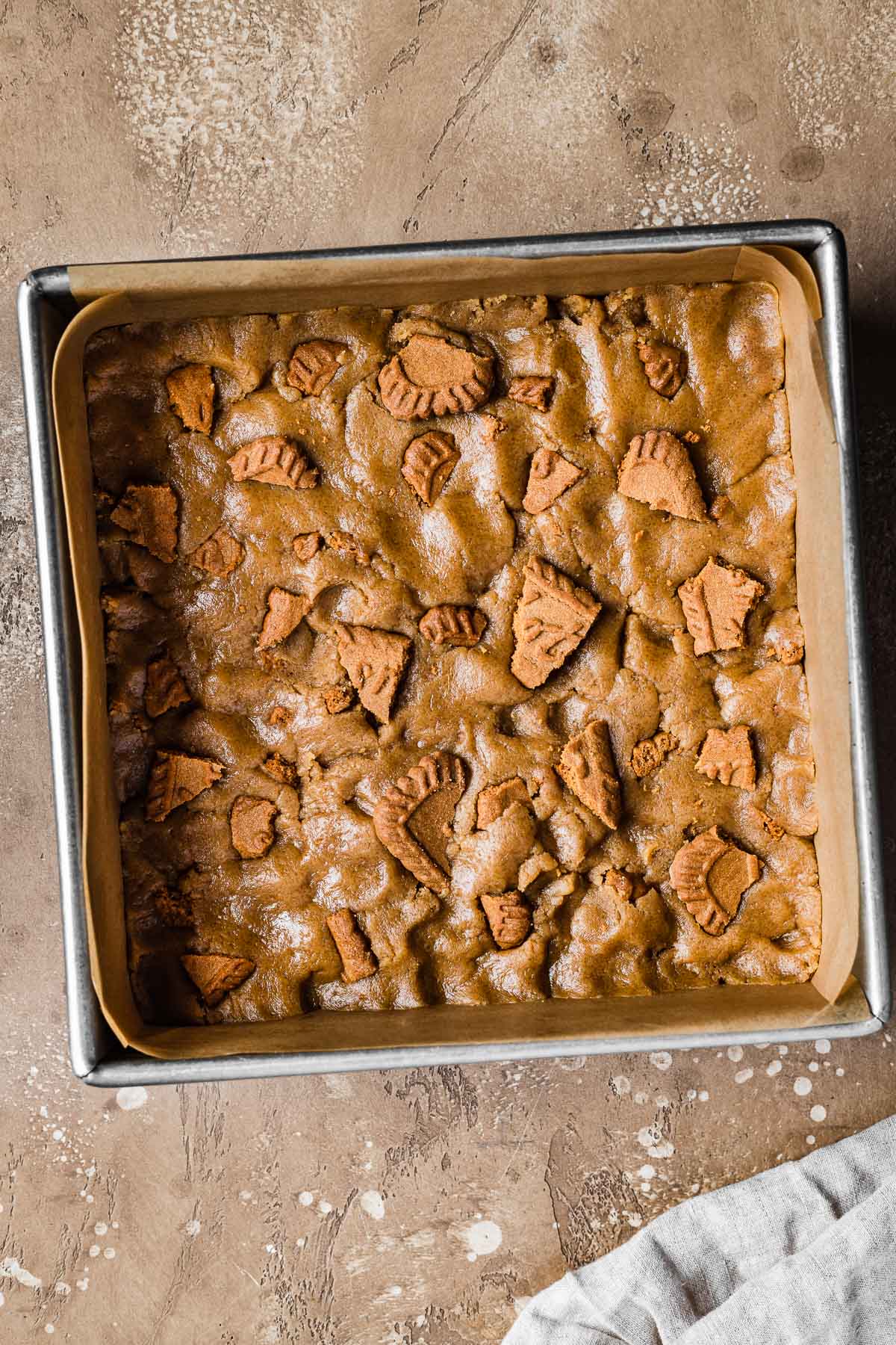 Dough for bar cookies patted into a parchment lined square baking pan.