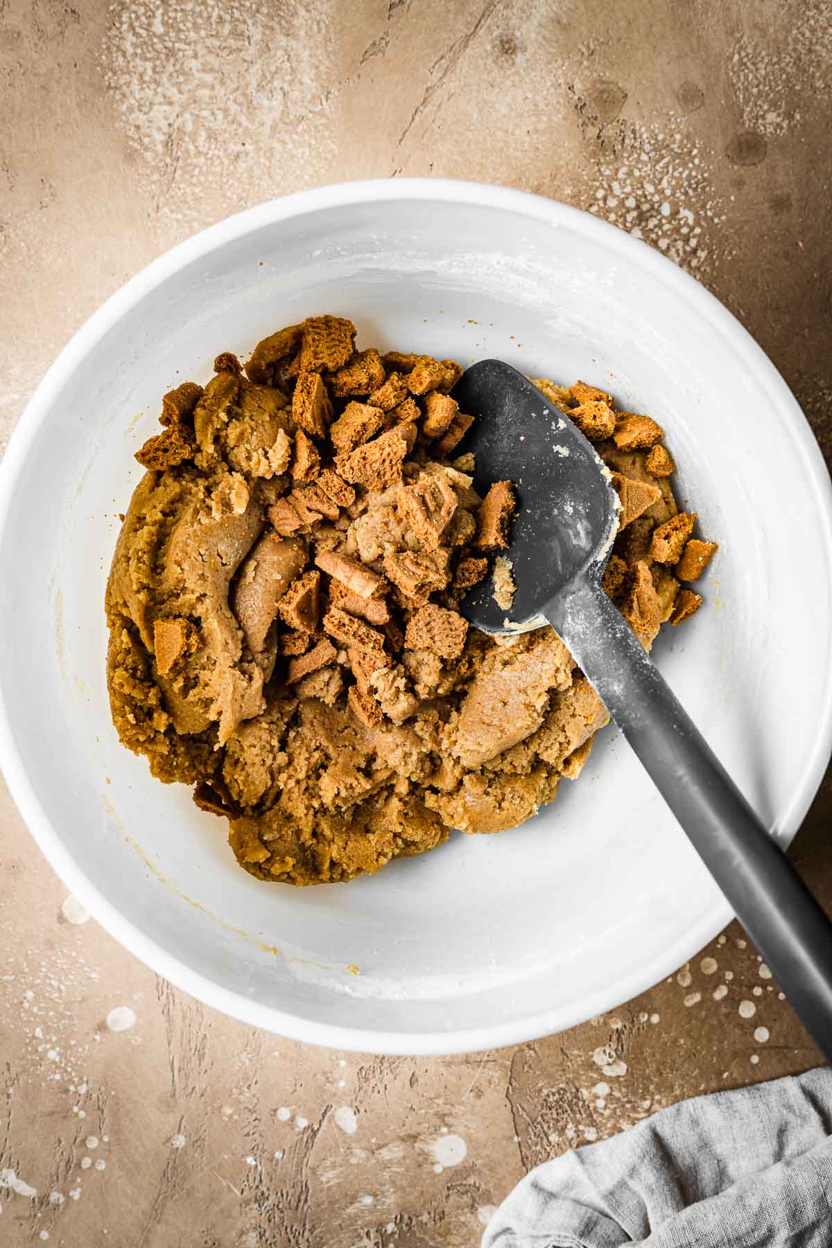 Broken up biscoff cookies in a white ceramic mixing bowl with dough.