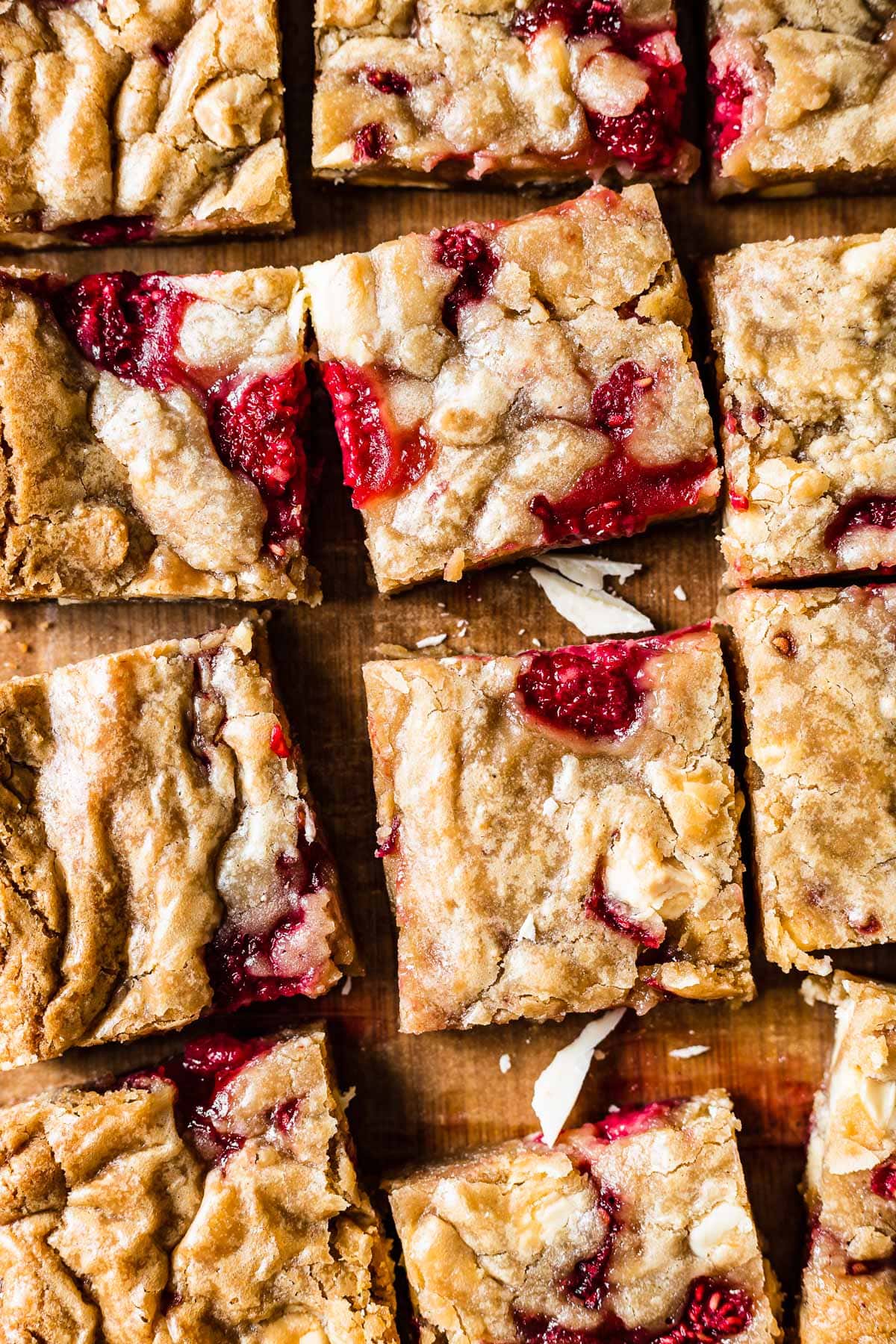 Squares of blondies studded with raspberries and white chocolate on a wooden cutting board.