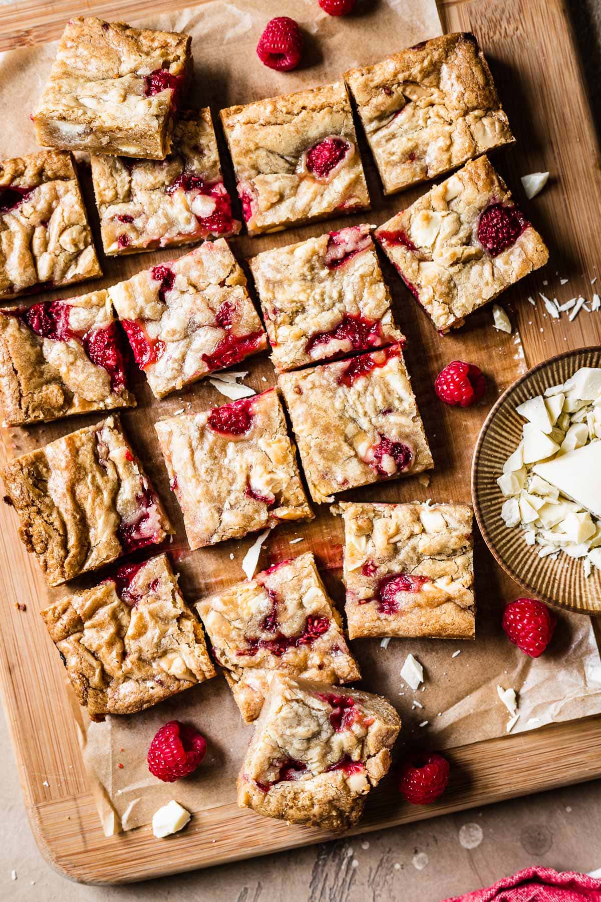 Raspberry white chocolate blondie squares on a wooden cutting board.