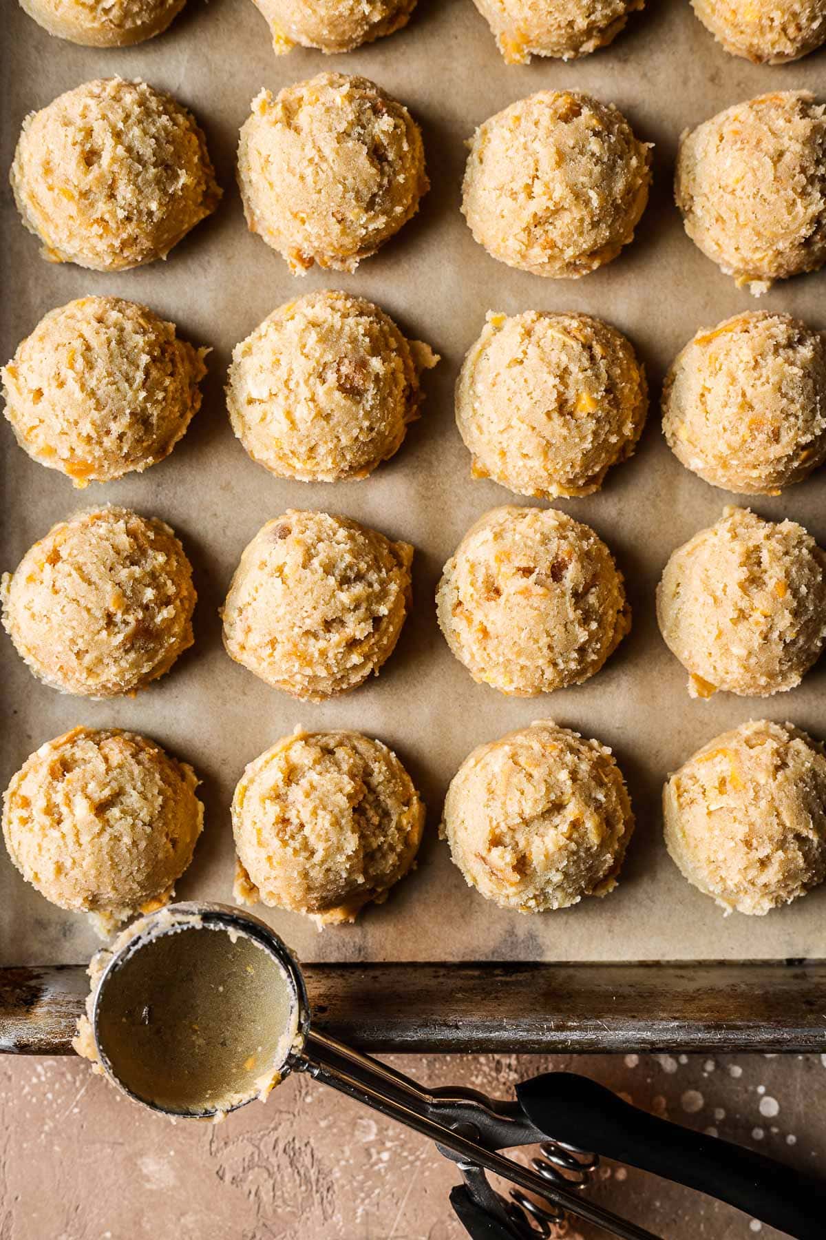 Scoops of mango cookie dough on a parchment lined baking sheet.