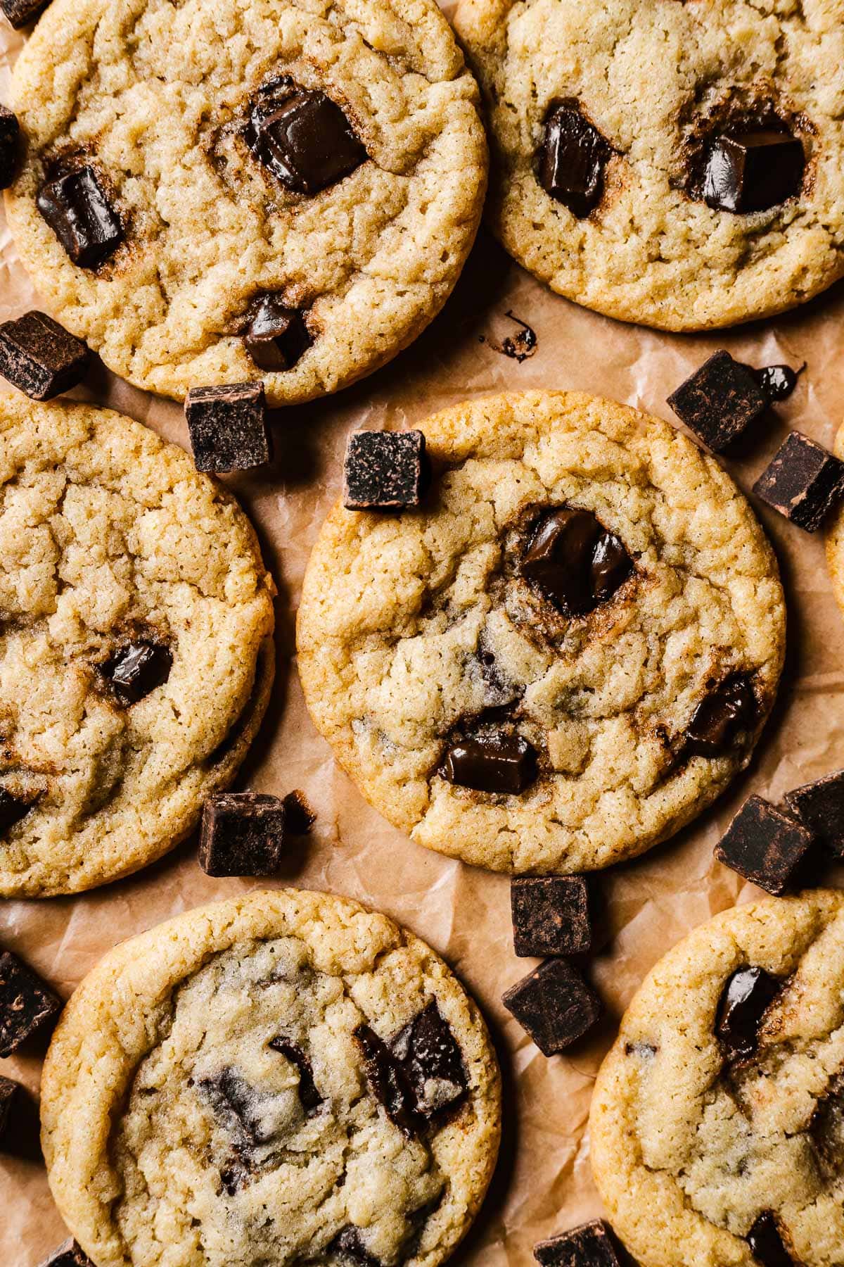 Eggless chocolate chip cookies on brown parchment paper with chocolate chips sprinkled amongst them.