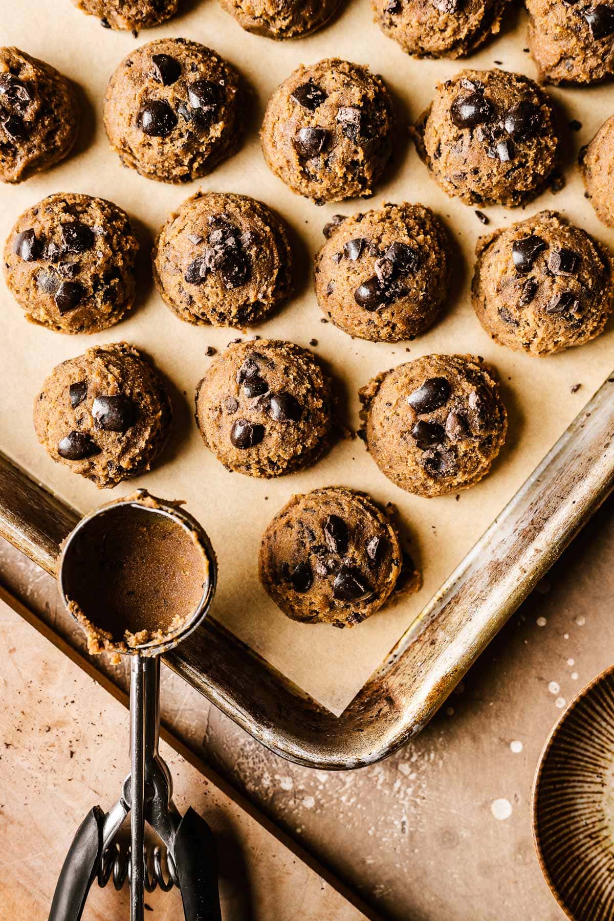 Scoops of coffee cookie dough on a parchment lined cookie sheet with chunks of chocolate coffee beans on top.