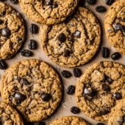 Coffee cookies on a tan surface with coffee beans sprinkled amongst them.