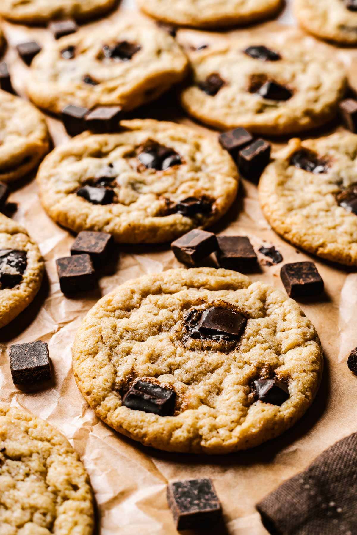 Cookies on brown parchment paper with chocolate chunks sprinkled amongst them.