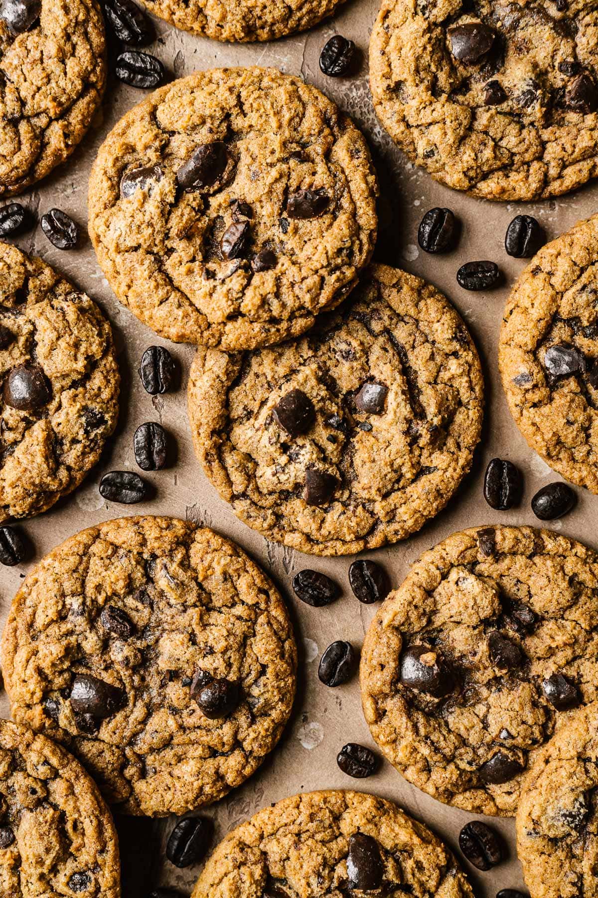 Coffee cookies on a tan surface with coffee beans sprinkled amongst them.