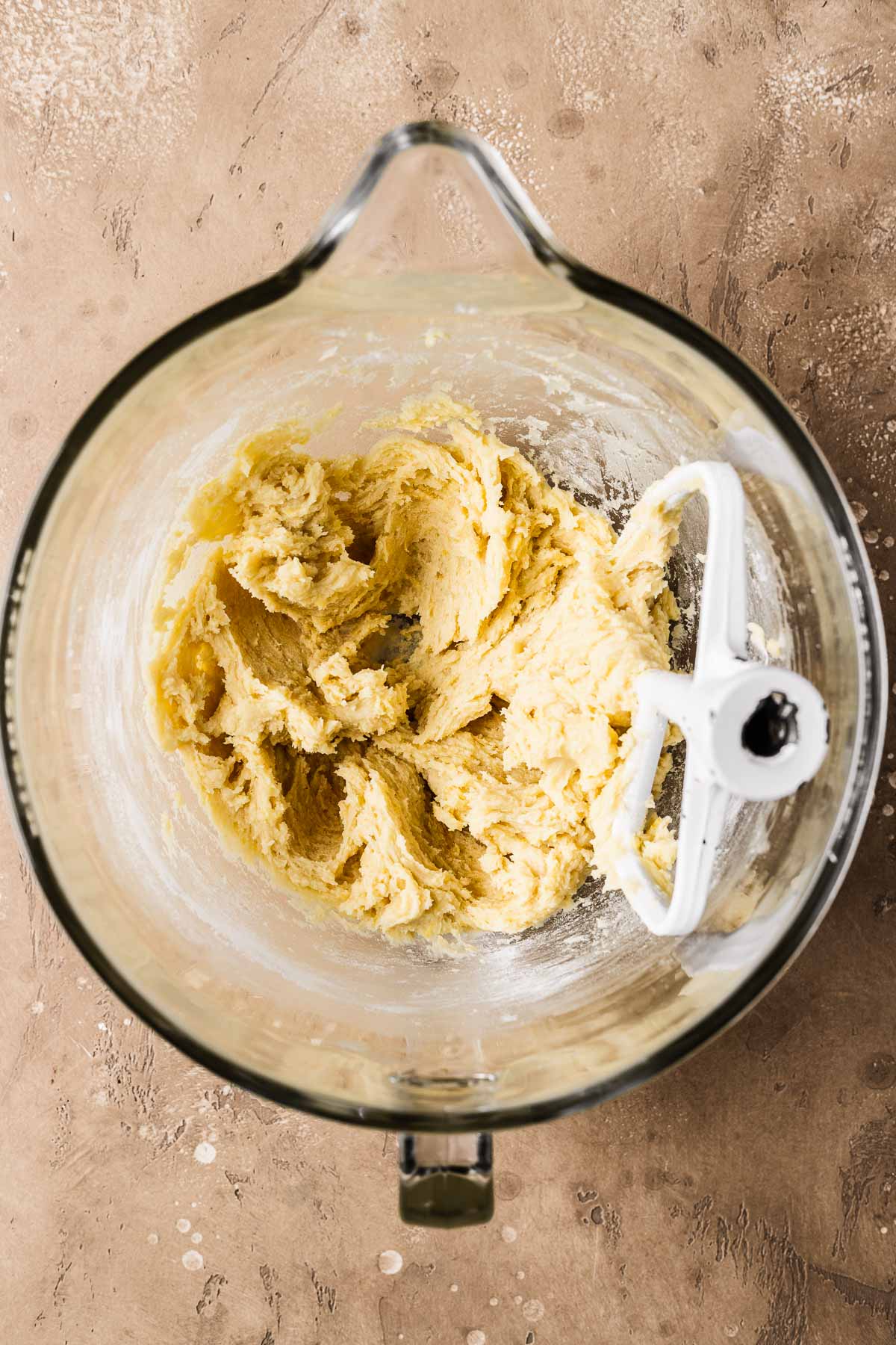 A clear glass mixing bowl of lemon white chocolate cookie dough with dry ingredients added.