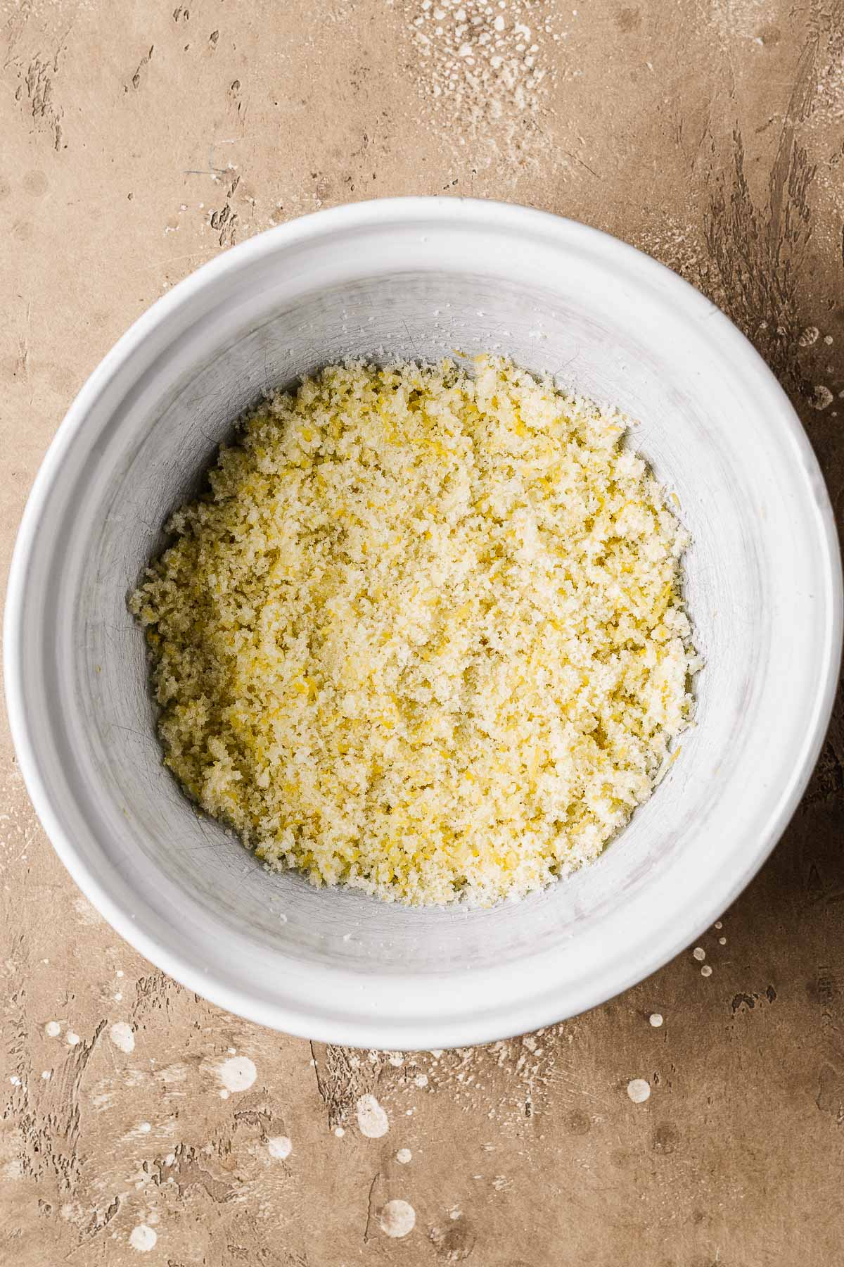 A white ceramic bowl of lemon zest mixed with granulated sugar.