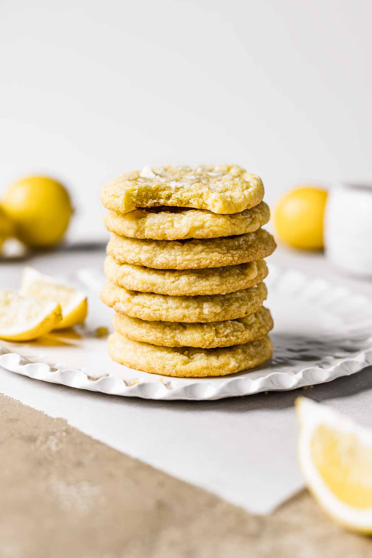 A stack of seven pale yellow lemon cookies on a white fluted plate.