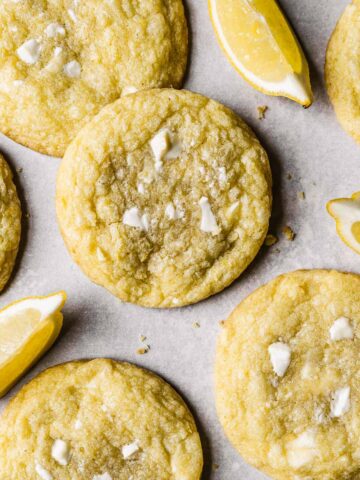 Lemon white chocolate cookies with lemon slices in between on white parchment paper.